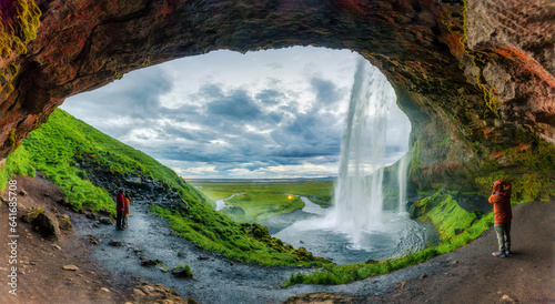 Natural cave with Seljalandsfoss waterfall flowing and tourist enjoying in summer at Iceland