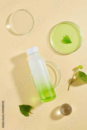 On the beige background, a glass ball, fresh leaves and a bottle are arranged. Branding mockup with empty label. Organic skin care of Fish mint (Houttuynia cordata) extract