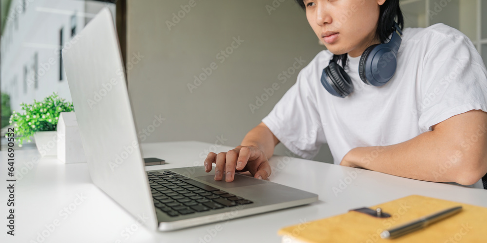 Asian young man using laptop while relax sitting at the table Asian young man using laptop while relax sitting at the table
