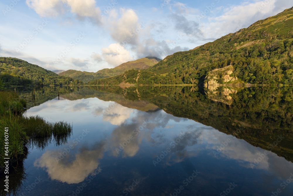 Beautiful calm and tranquil lake reflecting the surrounding clouds, forests and mountains at Llyn Gwynant, Snowdonia, Wales