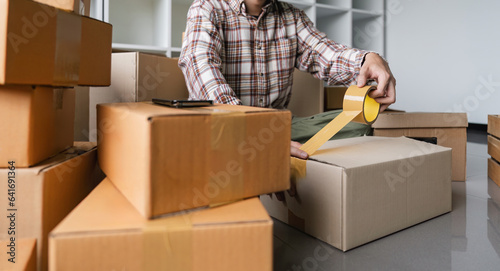 Concept young man moving house. Close up hand of man use tape sealing cardboard box © Natee Meepian