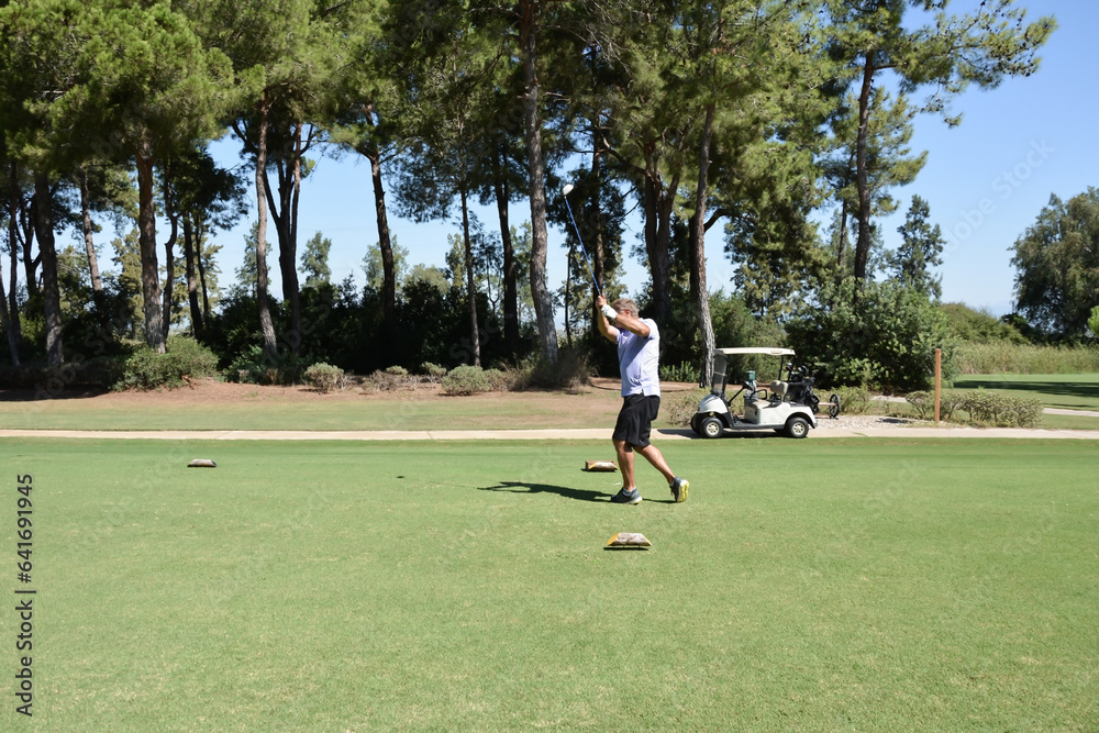 Obraz premium A man hits a golf ball with a club on the green of a private golf club. Active summer luxury vacation