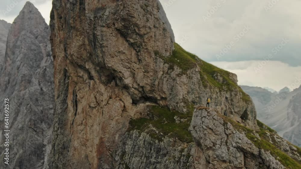 Aerial courageous hiker woman standing on the epic mountain rock peak of Seceda Dolomites. Travel exploring Alps Dolomites Italy nature outdoor on a dramatic cloudy day Aerial courageous hiker woman standing on the epic mountain rock peak of Seceda Dolomites. Travel exploring Alps Dolomites Italy nature outdoor on a dramatic cloudy day