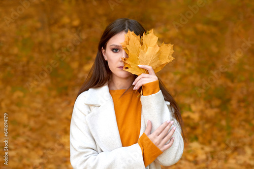sad woman wearing autumn coat walking at park. offended girl holding leaves bouquet in fall nature