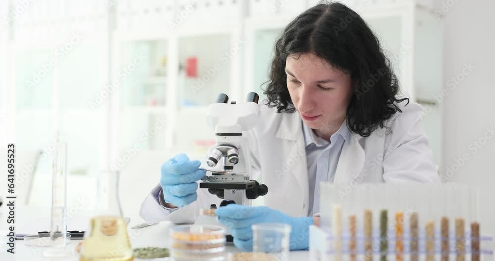 Concentrated male assistant making discovery while looking through microscope in lab. Chemist discouraged by results of experiment at work Concentrated male assistant making discovery while looking through microscope in lab. Chemist discouraged by results of experiment at work