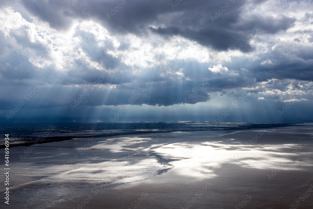 A wide-angle shot of the sun shining through clouds onto the land and sea beach. represents the power of nature. The sun is the power of life. The light from the sun nourishes all living things.