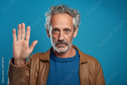 Close-up portrait photography of a tender mature man making a sorry gesture with hands together against a cerulean blue background. With generative AI technology