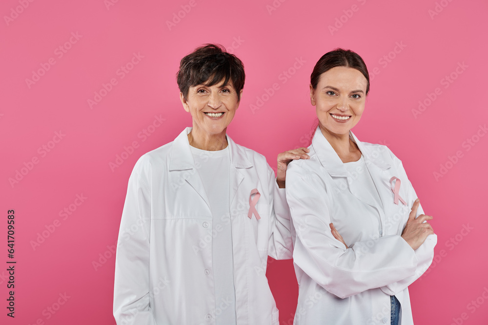positive doctors with ribbons posing and standing isolated on pink, breast cancer concept positive doctors with ribbons posing and standing isolated on pink, breast cancer concept