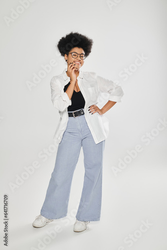 full length of stylish and smiling african american woman posing on grey background