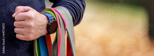 Strong man guy holding set of colorful elastic rubber bands at the stadium outdoors. Athlete male person during workout with additional sport equipmant photo