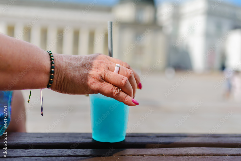 A woman holds a refreshing blue slushy in her hand at the summer city.