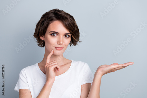 Photo of cute charming lady wear white t-shirt finger chin showing arm empty space isolated grey color background