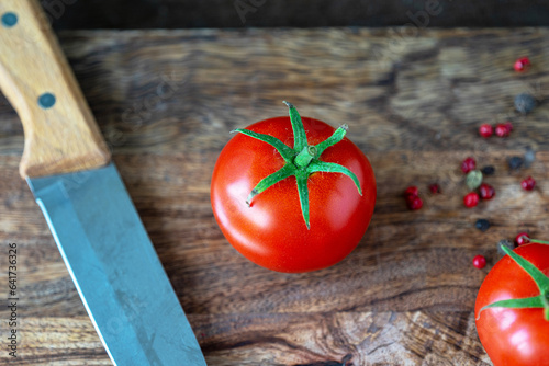 red tomato and kitchen knife on a dark wooden cutting board