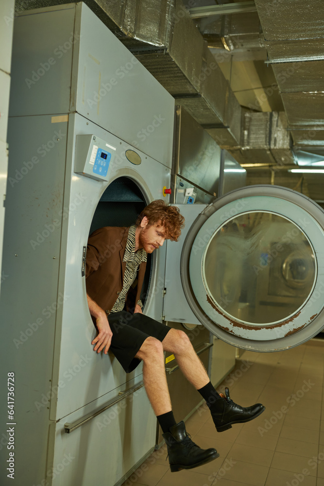 fashionable and modern man in jacket sitting in washing machine in coin laundry fashionable and modern man in jacket sitting in washing machine in coin laundry