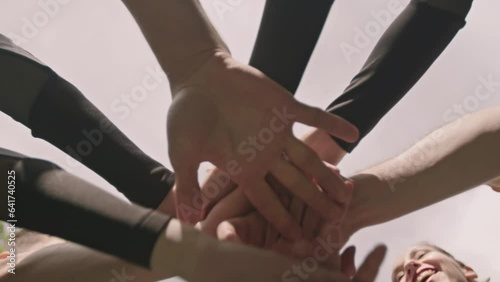 Directly below view of team of cheerleaders stacking hands and then raising arms up outdoors before sports match