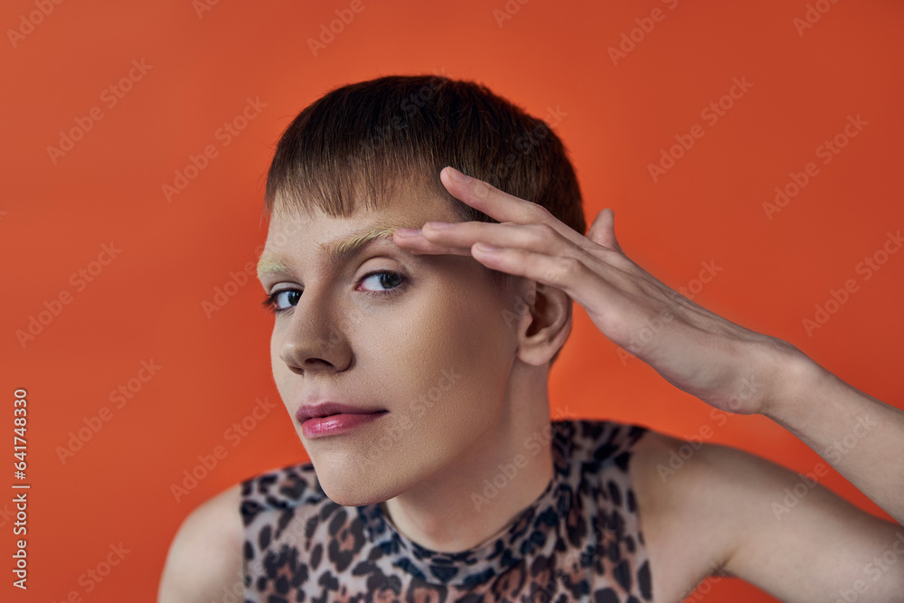 androgynous person smiling and looking at camera on orange backdrop, touching face, queer fashion androgynous person smiling and looking at camera on orange backdrop, touching face, queer fashion