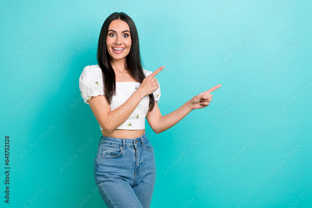 Photo of sweet excited girl dressed white top pointing two fingers empty space isolated teal color background Photo of sweet excited girl dressed white top pointing two fingers empty space isolated teal color background