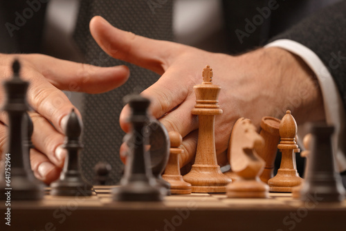 The male chess player's hand throws pieces off the chessboard. Shallow depth of field
