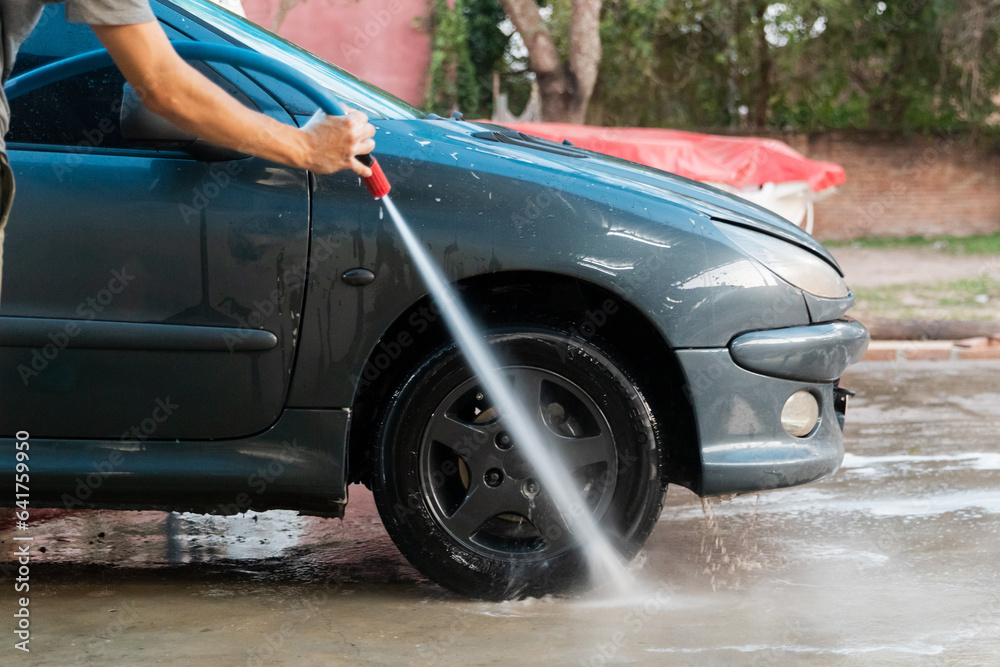 Side view of a man washing the car with a hose.