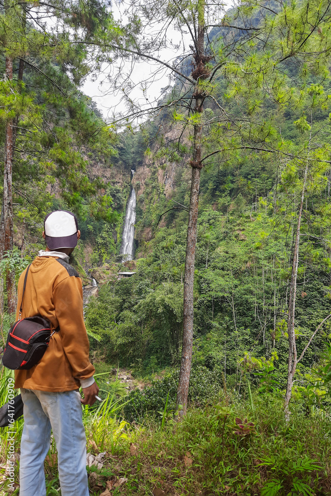 Man standing looking at the waterfall from a distance