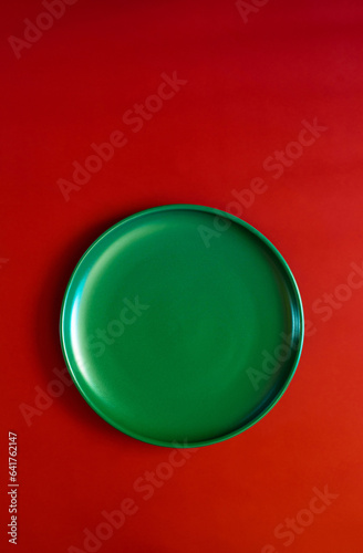 Green plate on a red background. Minimalistic concept of the winter holidays - Christmas and New Year. Top view. Space for text