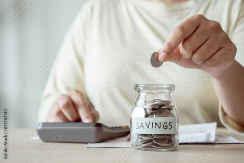 A woman's hands placing coins into a glass jar, the act of saving money to pay bills.