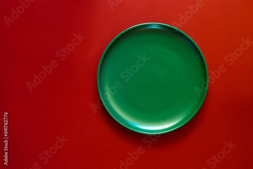 Green plate on a red background. Minimalistic concept of the winter holidays - Christmas and New Year. Top view. Space for text