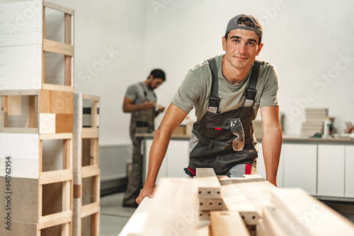Leinwand Poster Portrait of young male carpenter standing in the wood workshop