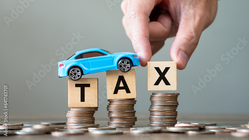 Concept of car tax.Hand holding tax wooden text with toy car on stack coins.Saving and manage money for transport,economic crisis risk and problem concept. photo