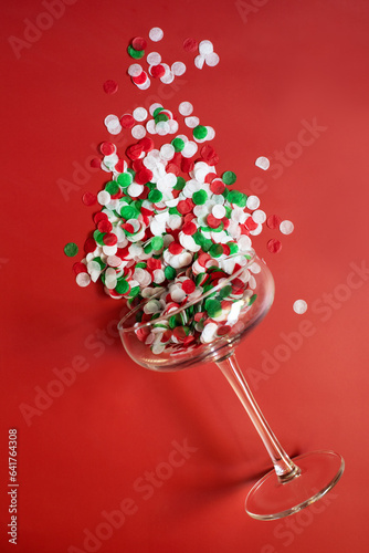 Confetti in a champagne glass on a red background. The concept of the winter holidays - Christmas and New Year. Top view. Space for text