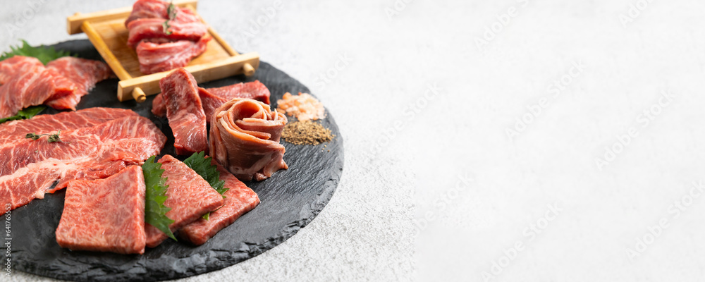 Top view Variety Fresh raw beef steaks on natural black stone plate for grilling. hot pepper and herbs. Japanese food isolated on gray stone banner background