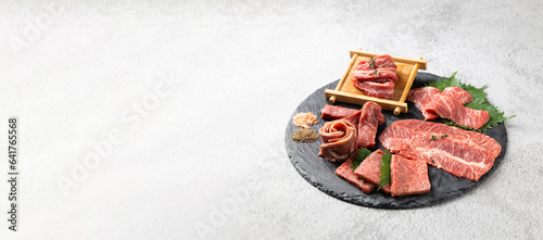 Top view Variety Fresh raw beef steaks on natural black stone plate for grilling. hot pepper and herbs. Japanese food isolated on gray stone banner background