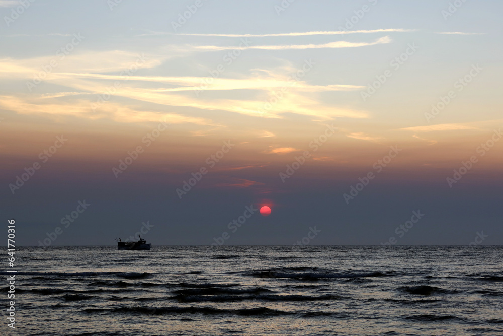 Scenic sunset over the sea. Touristic ship sailing through the sea. Poland seaside, Leba village and beach. Seascape