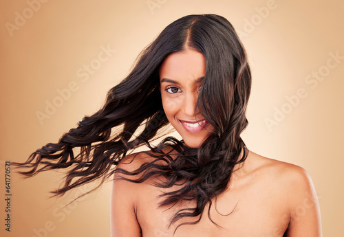 Portrait, woman and curly hair in wind on studio background for shine, beauty and keratin shampoo. Happy indian model, hairstyle and waves in breeze for aesthetic texture, growth and salon cosmetics