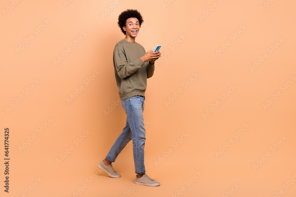 Fototapeta premium Full length body photo cadre of positive good mood guy stylish outfit hold cellphone read information walk street isolated on beige color background