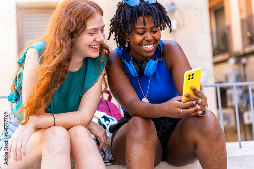 Interracial and multicultural friendship. Two friends looking at their cell phones on the street