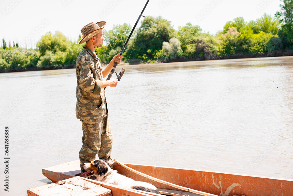 Slim man in camouflage standing at stern of boat, catching fish in calm ...