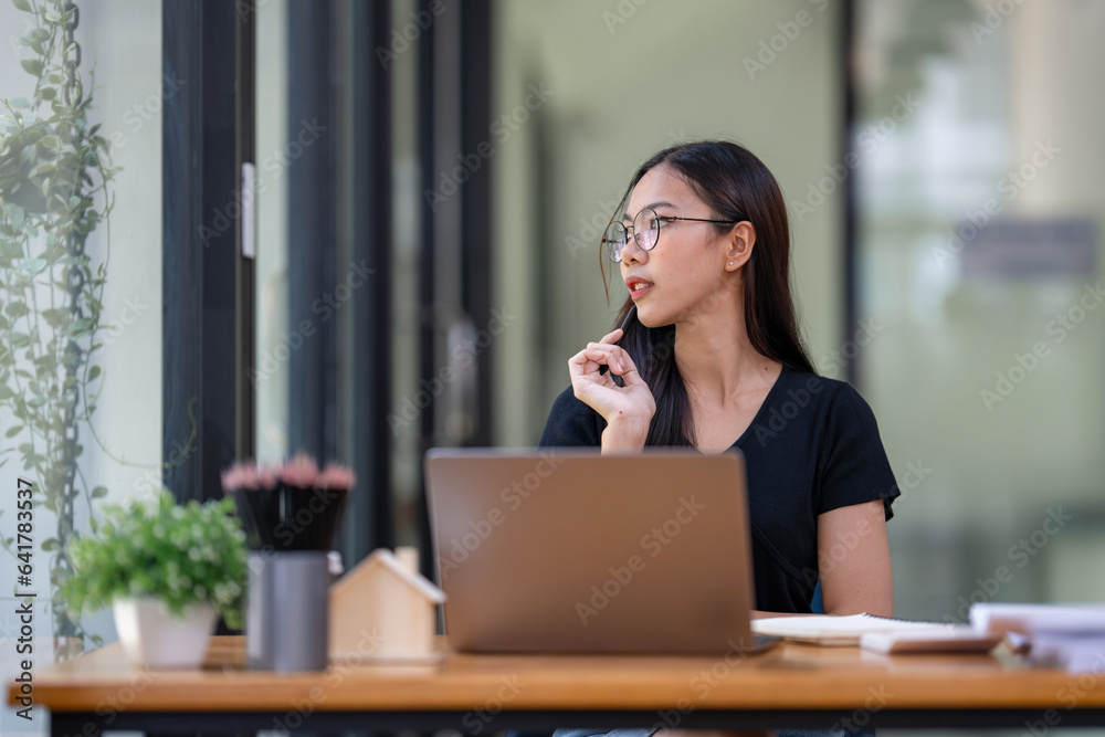 Freelance businesswoman wearing glasses uses laptop to search for information for project consideration, thinking work concept. Freelance businesswoman wearing glasses uses laptop to search for information for project consideration, thinking work concept.