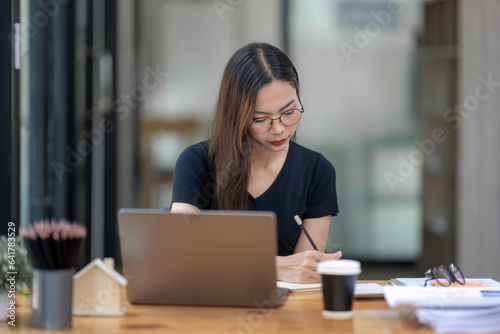 Freelance businesswoman wearing glasses uses laptop to search for information to write a project plan.