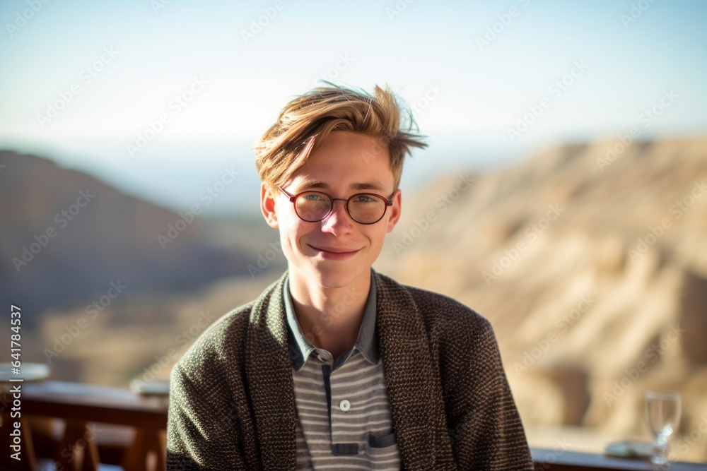 Photography in the style of pensive portraiture of a grinning boy in his 30s wearing a chic cardigan at the masada in southern district israel. With generative AI technology