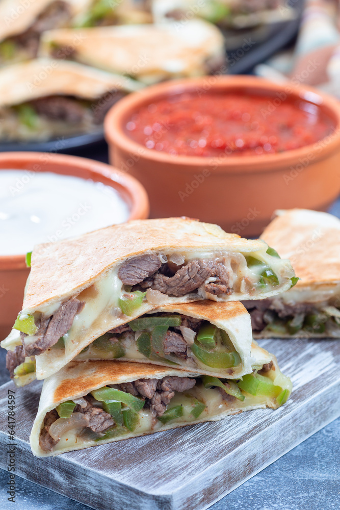 Mexican fajita quesadilla with pieces of beef steak, bell pepper, onion and cheese, on wooden board Mexican fajita quesadilla with pieces of beef steak, bell pepper, onion and cheese, on wooden board