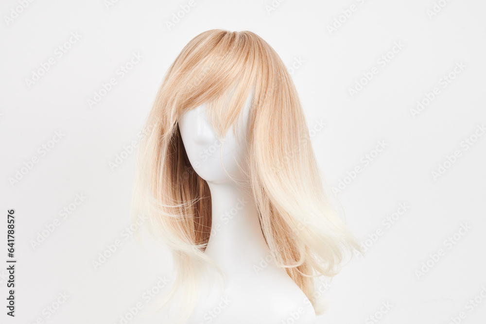 Naklejka premium Natural looking blonde wig on white mannequin head. Long hair on the plastic wig holder isolated on white background.