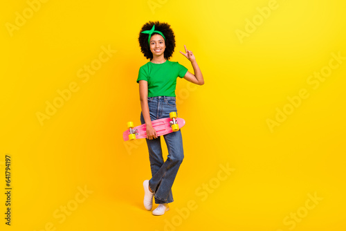 Full body portrait of cheerful friendly schoolgirl hold skateboard empty space isolated on yellow color background