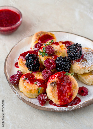 Cheesecakes served in a ceramic plate, with raspberries and blackberries, sprinkled with honey and raspberry jam, sprinkled with powdered sugar.