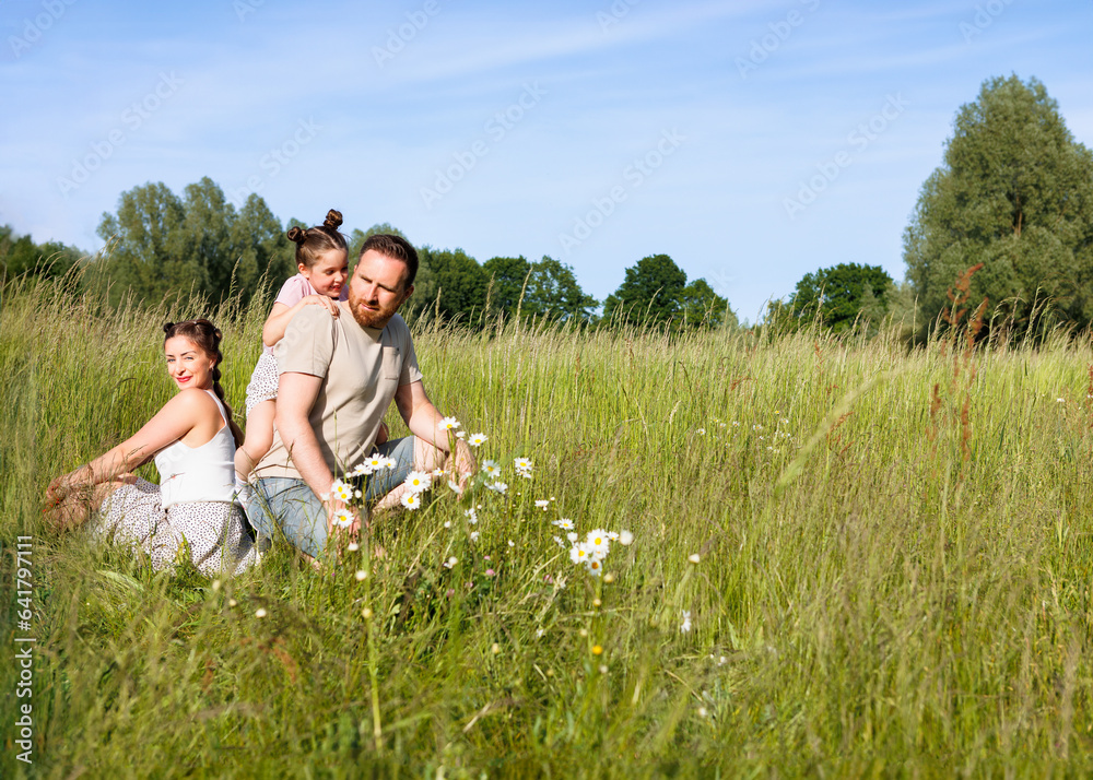Summer sunny day for a young family, dad, mom and little girl became joyful and happy. Beautiful flower meadow, happy family concept.