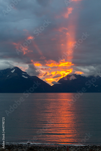 Lake with illumination of the sun in the clouds rising between mountains at sunset