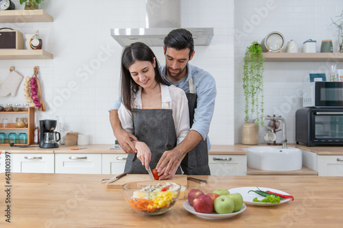 Happy couple preparing food at home  young couple cutting vegetables together at kitchen counter