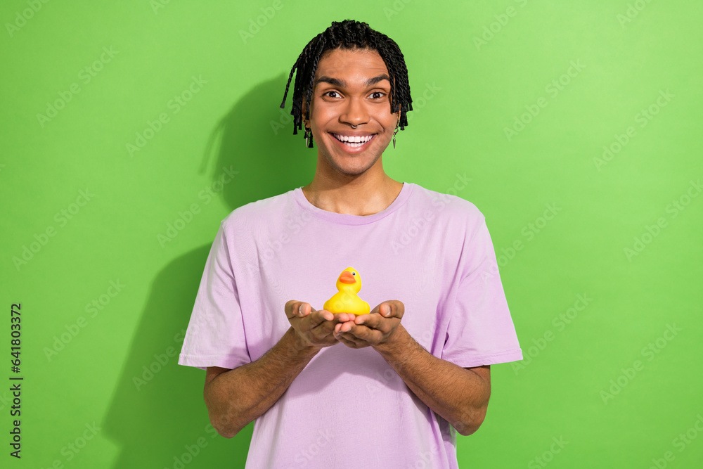 Photo of childish overjoyed person toothy smile arms palms hold small rubber bath duck toy isolated on green color background Photo of childish overjoyed person toothy smile arms palms hold small rubber bath duck toy isolated on green color background