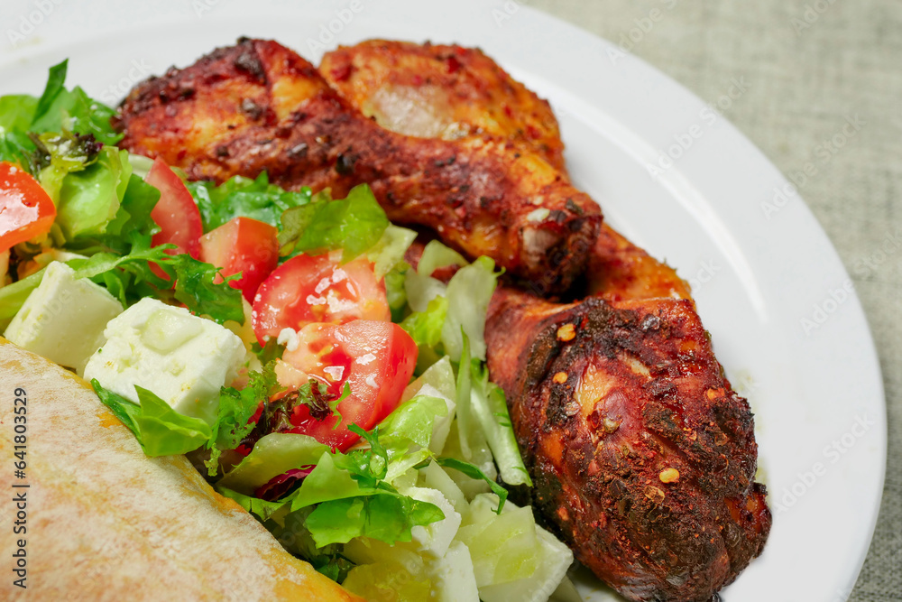 Cooked meal on a plate with marinated chicken drumsticks and fresh salad and Italian bread. Mediterranean style food. Selective focus. High quality product. Healthy eating.