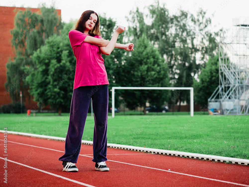 Young teenager girl doing stretching exercises on a running track. Selective focus. The model is slim body type. Light and airy look. Get ready for sport concept. Outdoor activity and lifestyle.